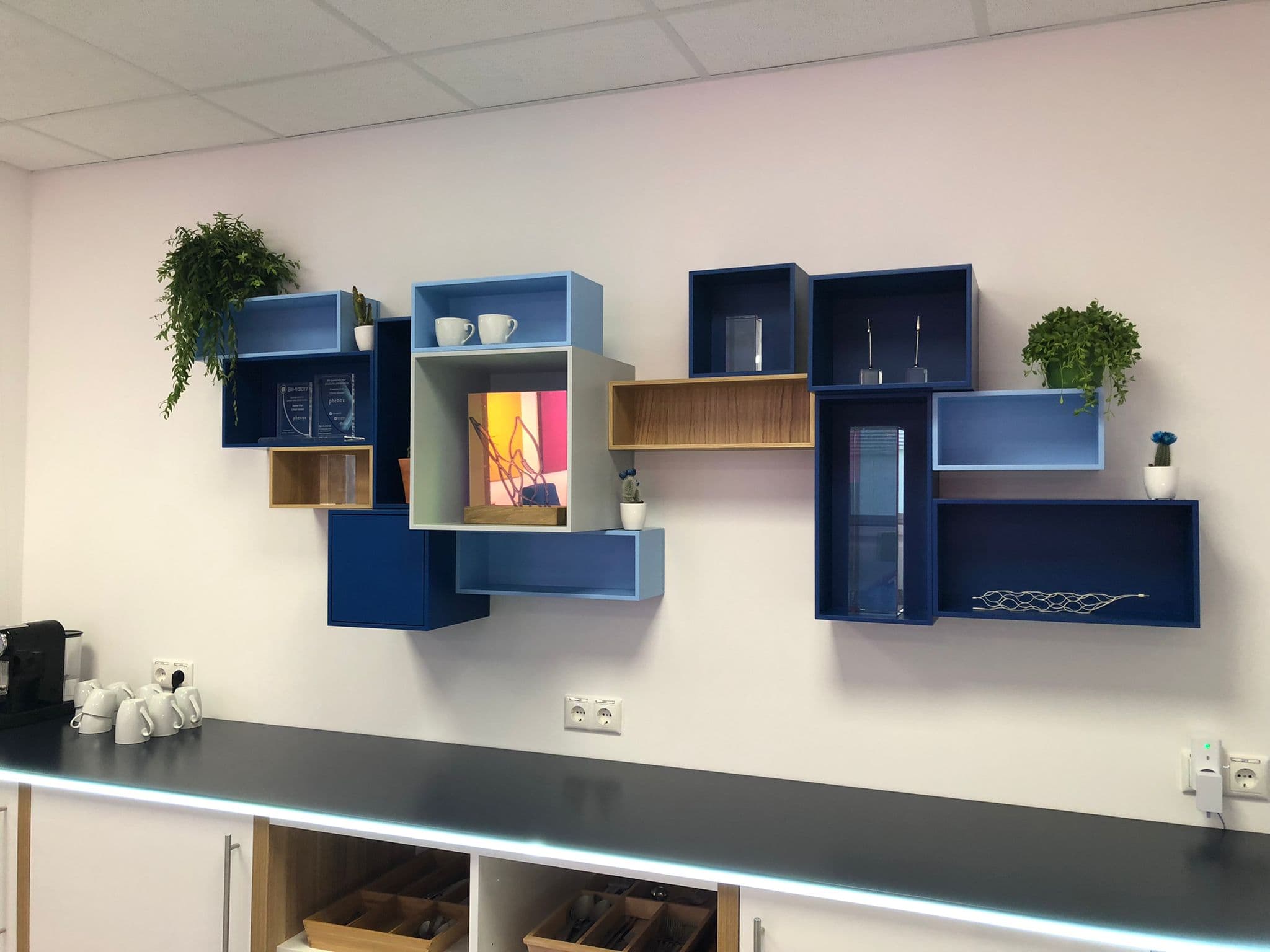 Eine Wand mit bunten, geometrischen Regalen, dekoriert mit Pflanzen und Tassen.