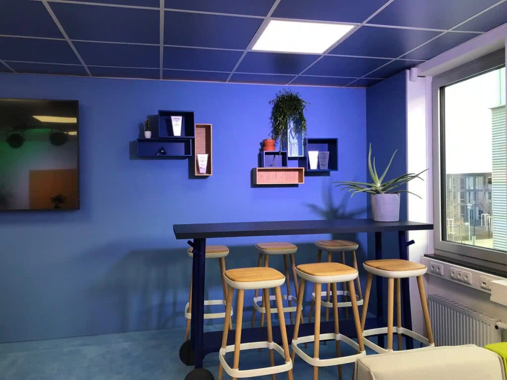 Moderner blauer Raum mit Barhockern und Pflanzen, Tageslicht durch Fenster.