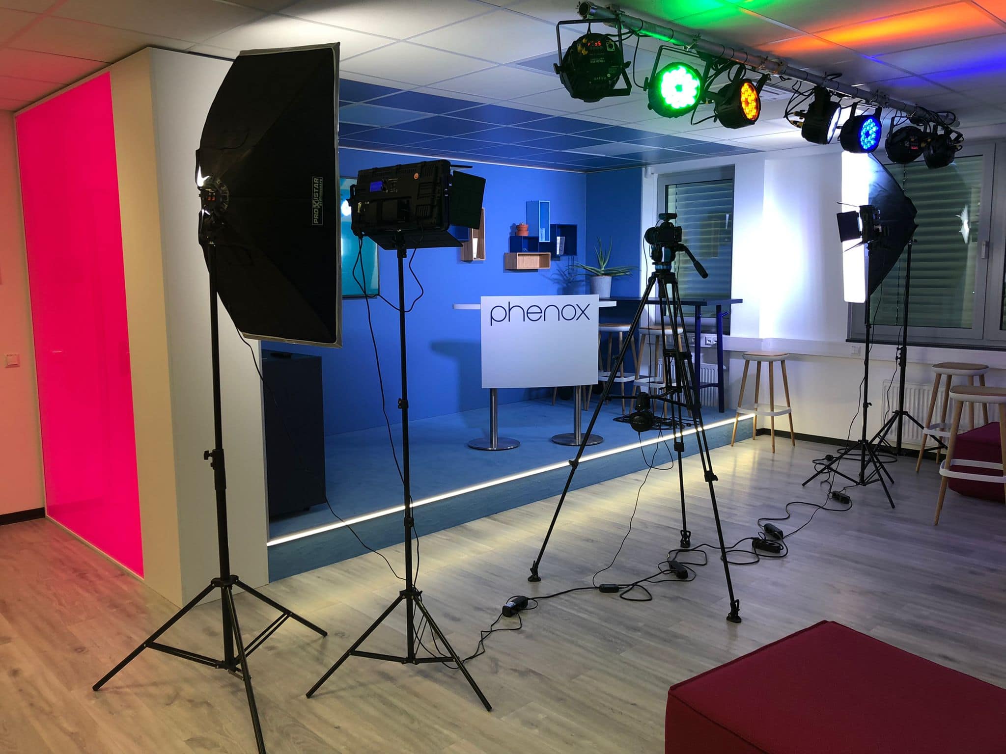 Ein modernes Aufnahmestudio mit bunter Beleuchtung und Kameraausrüstung vor blauer Wand.